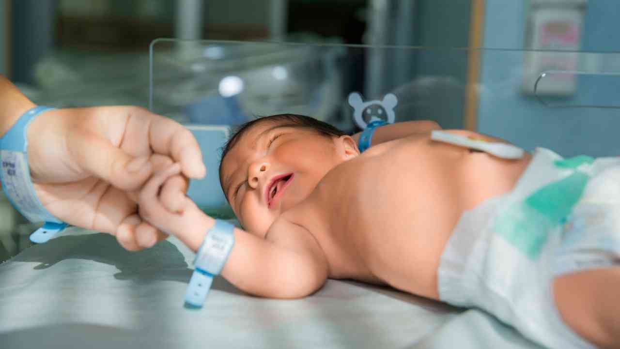 father holds hand newly born babe diapers