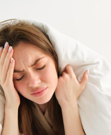 close-up-woman-feeling-unwell-home-lying-bed-white-blankets-frowning-touching_1258-193616