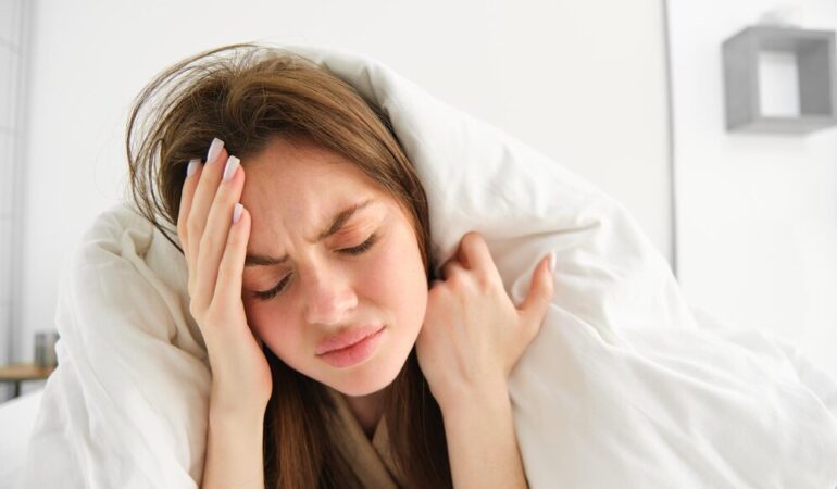 close-up-woman-feeling-unwell-home-lying-bed-white-blankets-frowning-touching_1258-193616