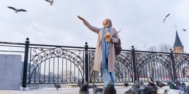 muslim-woman-feeding-pigeons-while-traveling-city_23-2149275774