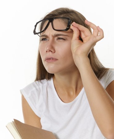 Picture of focused serious young Caucasian female teacher with textbook, taking off glasses and narrowing eyes, trying to see something clearly. Student girl in eyewear posing with diary in studio